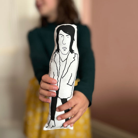 A child holding out a black and white screen printed cushion doll depicting Noel Fielding.