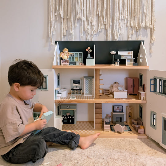 Child playing with a detailed dollhouse in a room with decorative elements.
