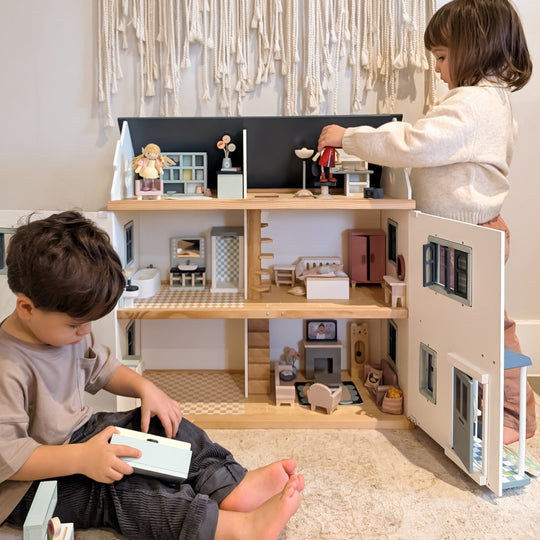 Two children playing with a dollhouse in a room with decorative elements.