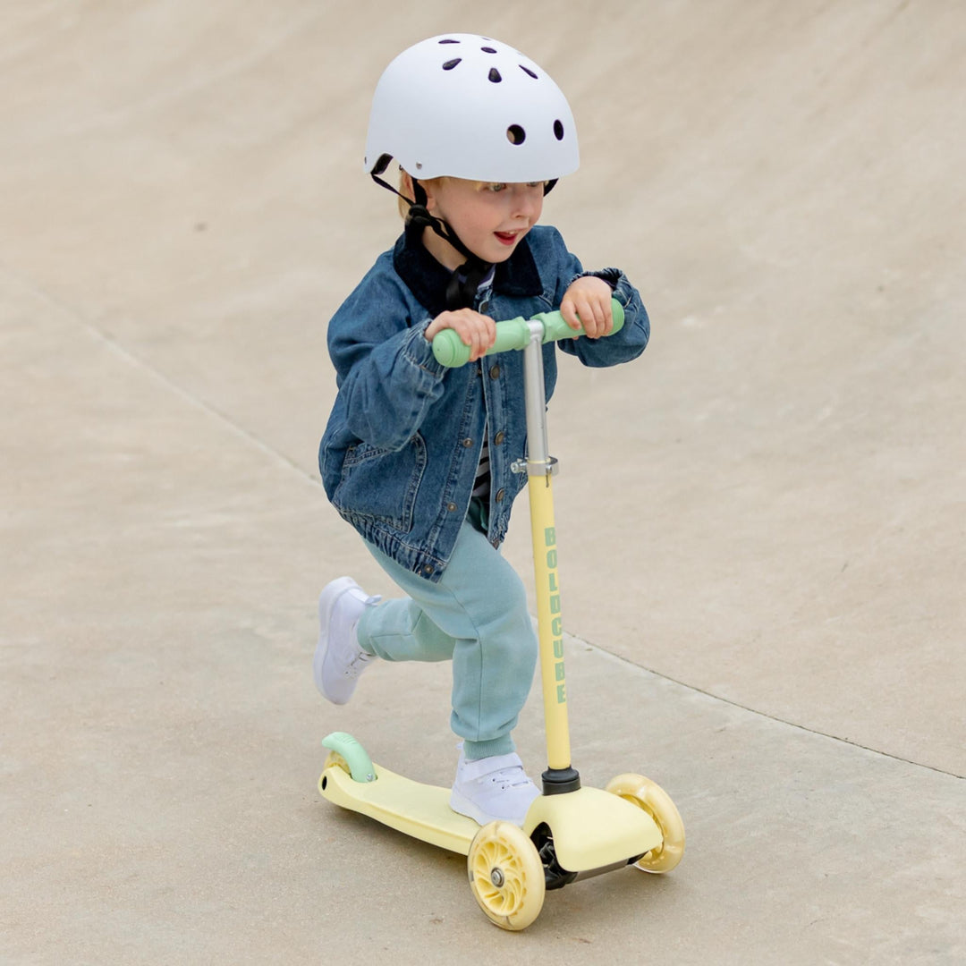 Child riding a yellow scooter on a beige pavement