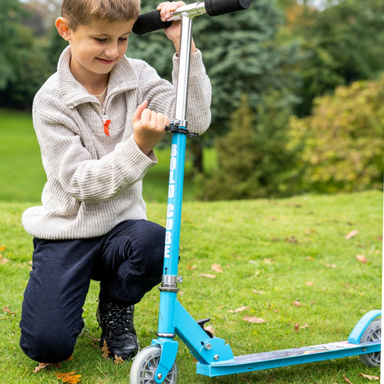Child playing with a blue scooter in a grassy outdoor setting showing the adjustable height handlebars
