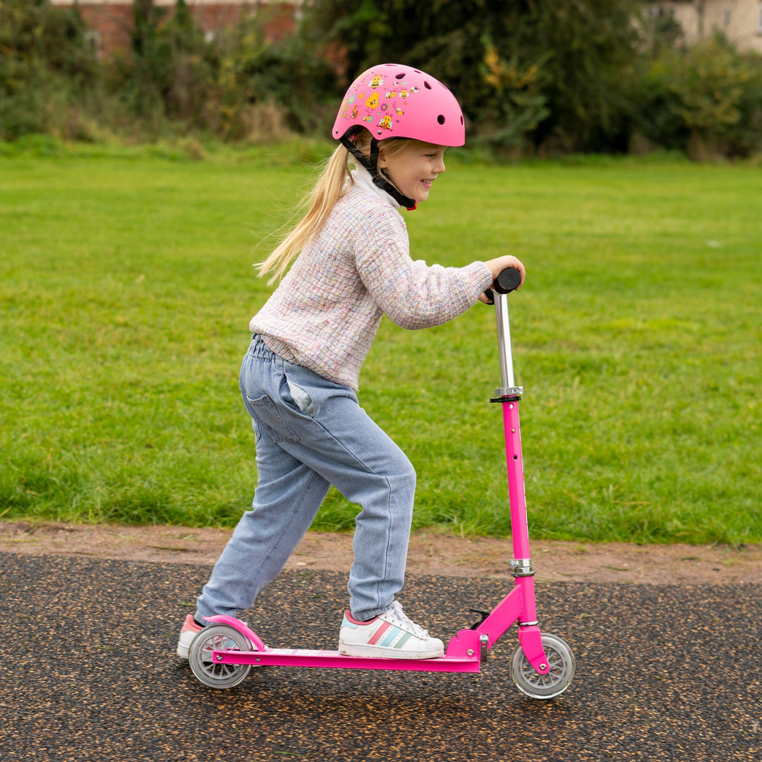 Child riding a pink scooter on a path with grass in the background