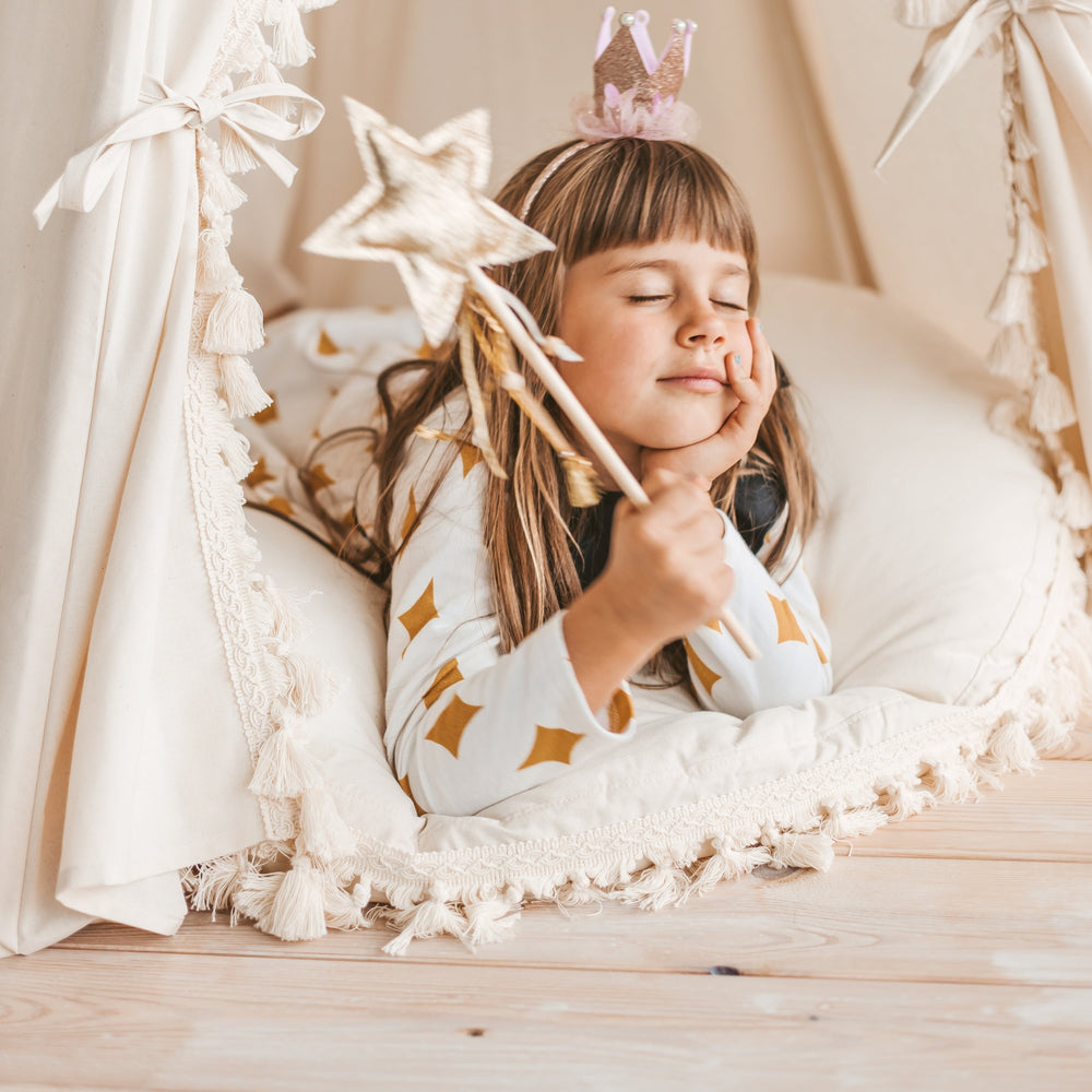 Child lying on a round floor cushion with a star-shaped wand, wearing a star-patterned shirt.