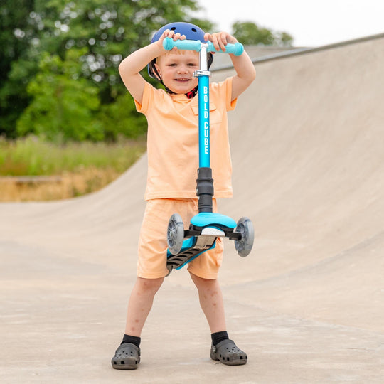 Child with a blue scooter on a paved path with greenery in the background