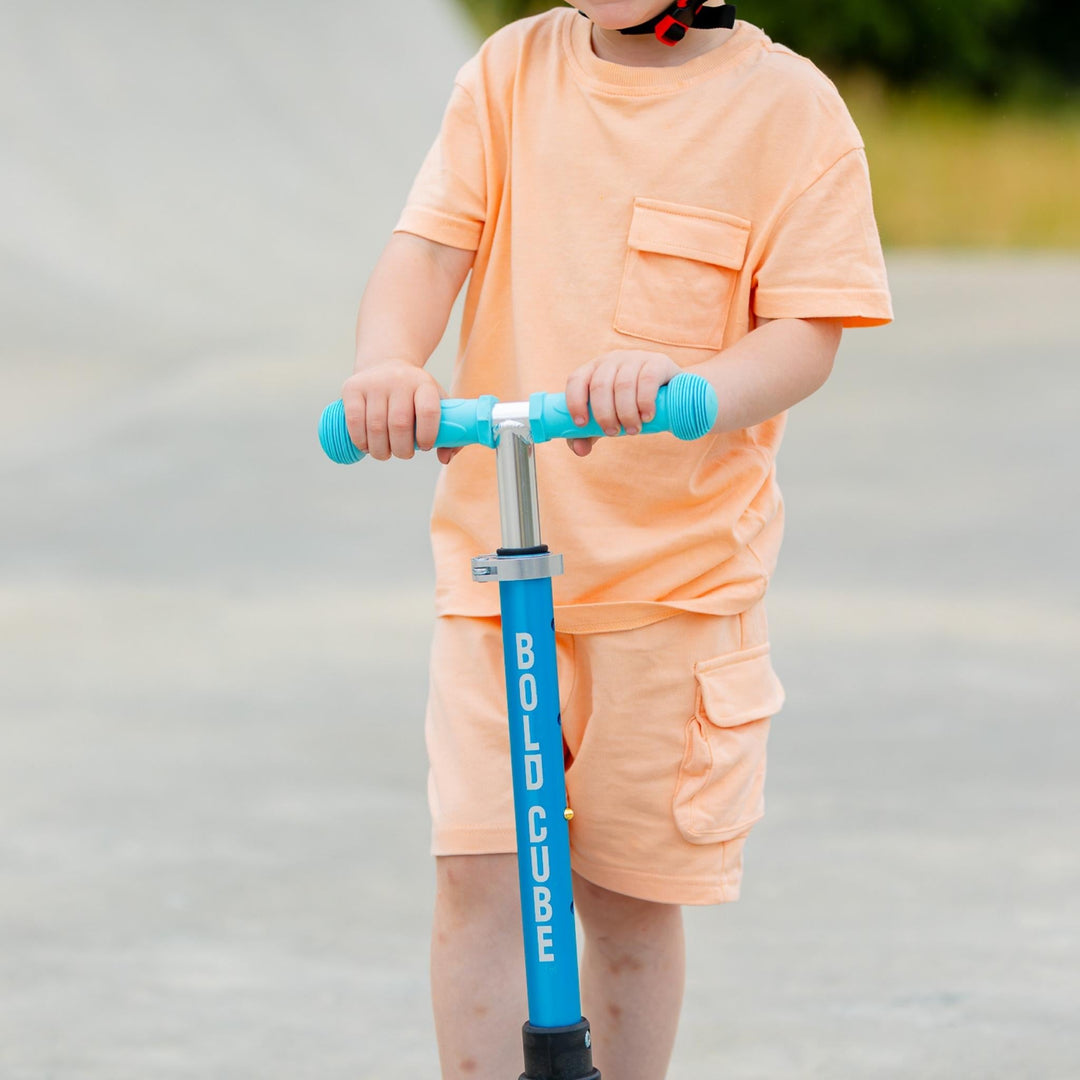 Child holding a blue pogo stick with 'BOLD CUBE' branding outdoors.