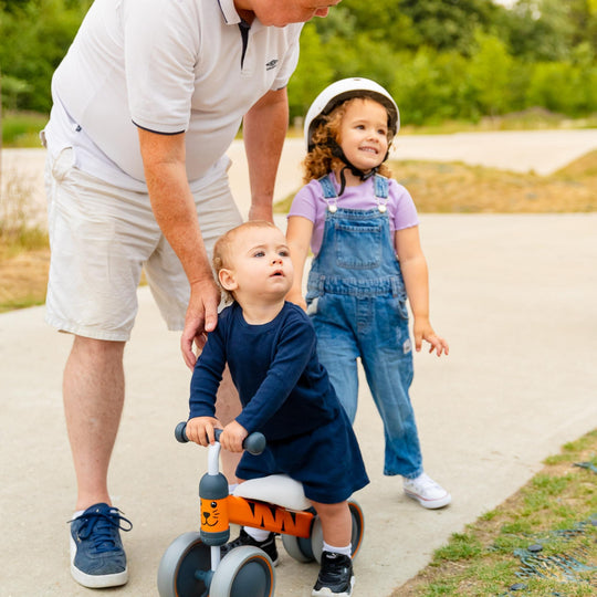 Two children on a bike with an adult nearby, outdoors.