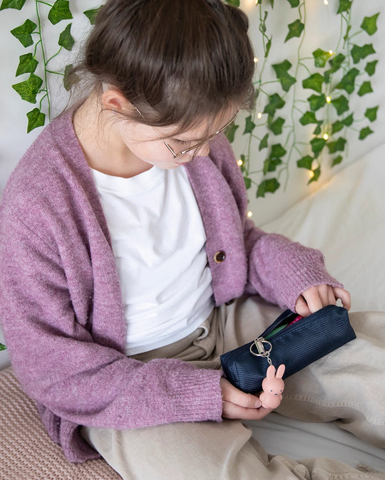 Child wearing a purple cardigan holding a pencil case with pink Miffy keyring attached to the zip