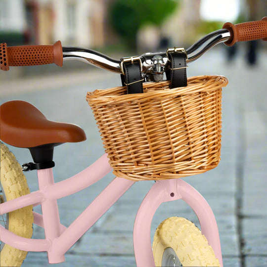 Close up of brown wicker basket attached to handlebar by black leather straps with silver buckles