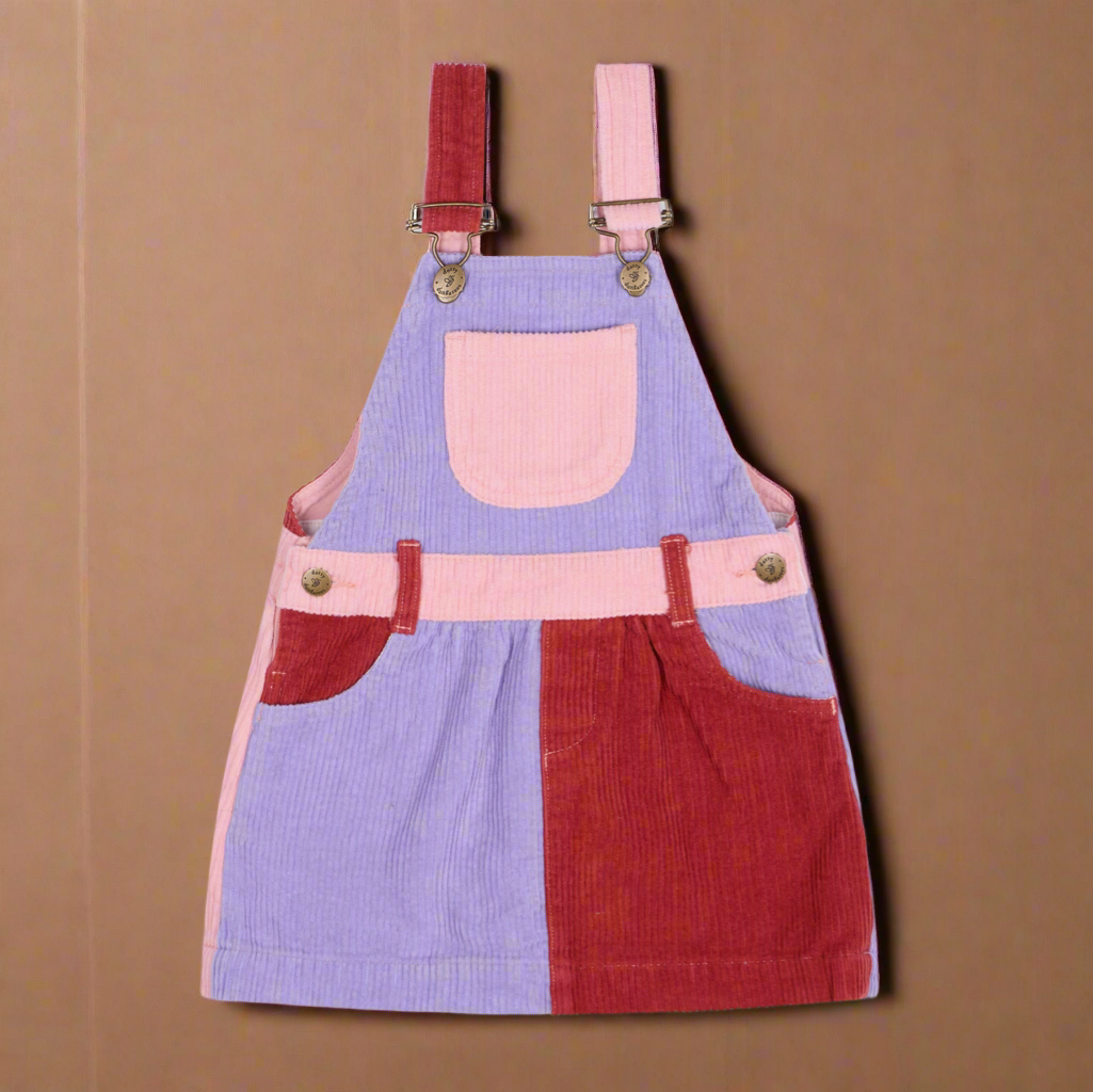 Corduroy patchwork dress with segments of pale pink, pale purple and red, with a pocket on the central chest and brass buttons