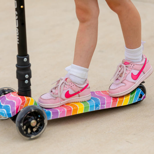Close up of child's feet on the tread of the scooter and one foot applying the brake which is ovee the back wheel
