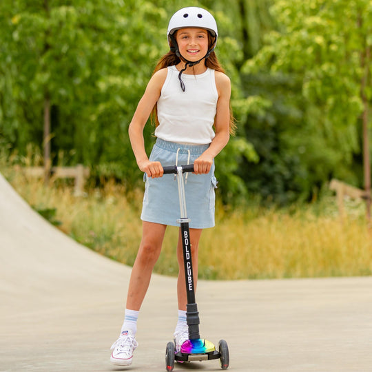 Girl riding a scooter with a helmet on a path surrounded by greenery