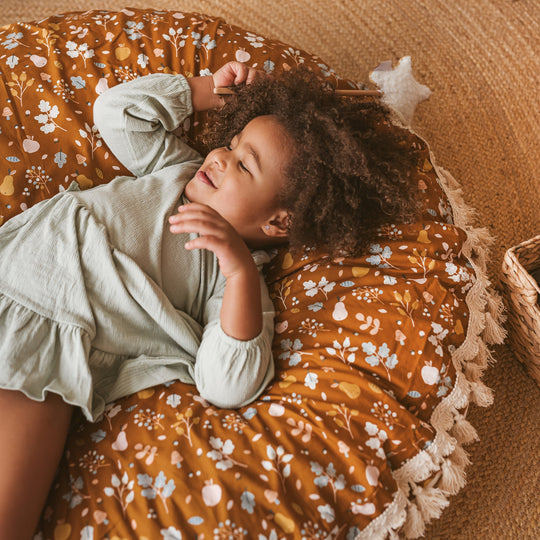 Child lying on a floral-patterned floor cushion with a soft, warm background
