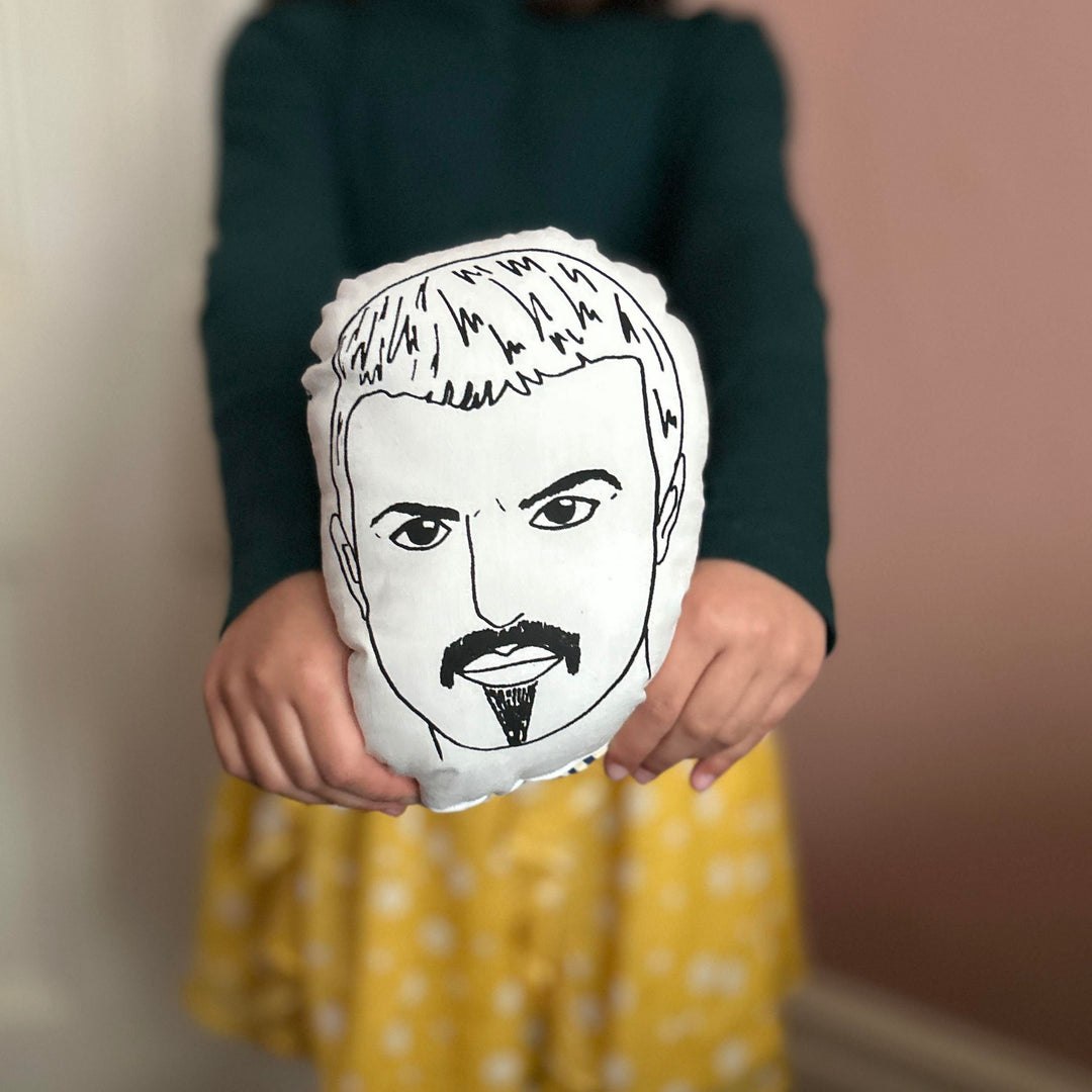 A child holding a monochrome screen printed cushion doll depicting the likeness of George Michael towards the camera