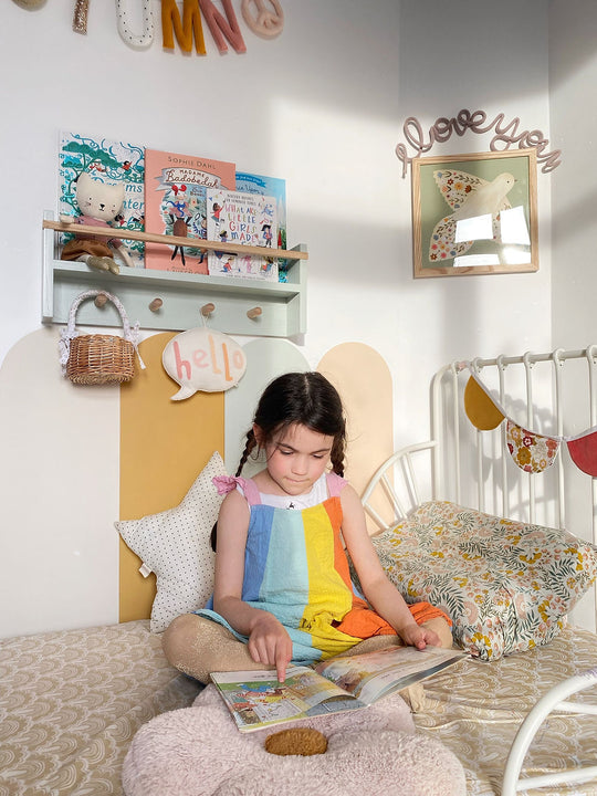 Child reading on a bed with booskhelf in background