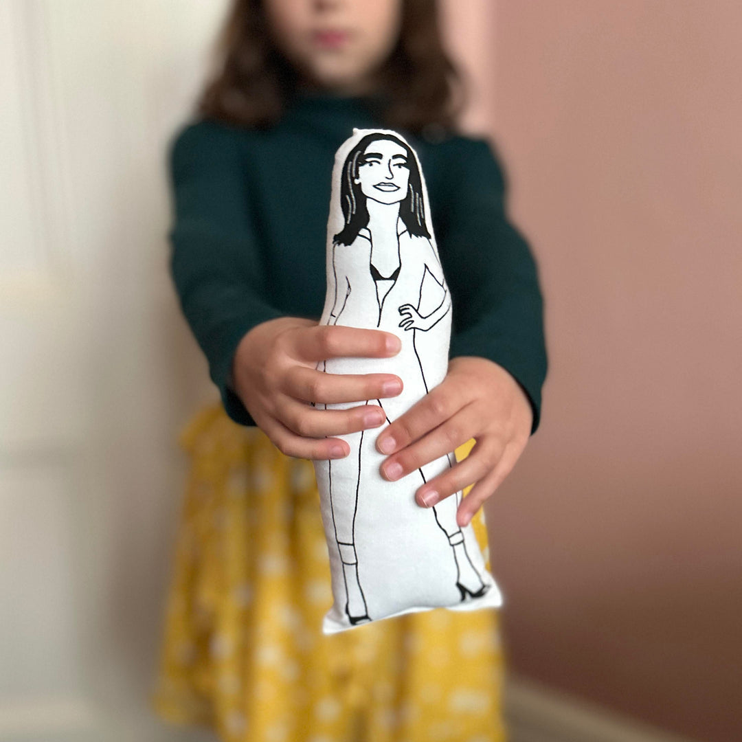 A child holding a screen printed fabric cushion doll with an illustration of PJ Harvey in her iconic cat suit.