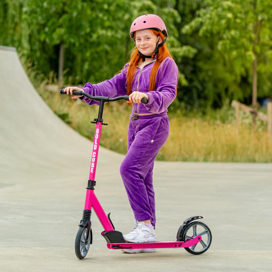 Child on a pink scooter with a helmet in an outdoor setting