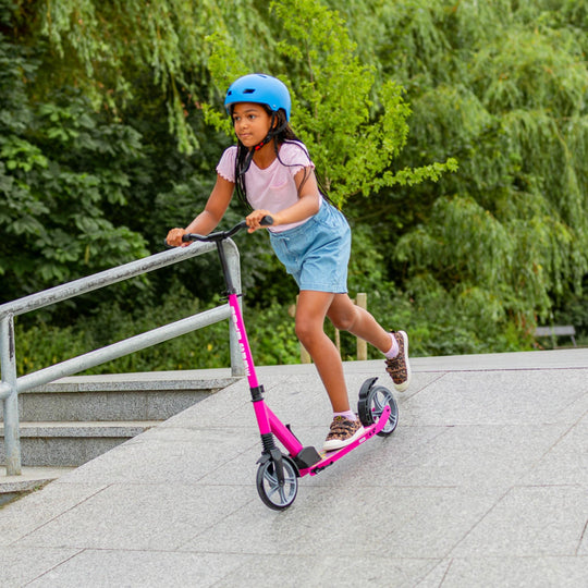 Child riding a pink scooter outdoors with greenery in the background