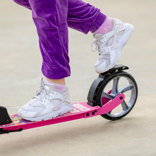 Close up of child's feet on the scooter with one foot applying the brake which is over the back wheel