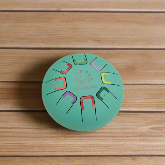 Round teal coloured metal tongue drum with colour-coded notes