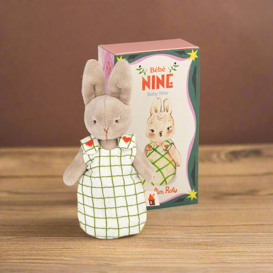 Plush rabbit toy in a white checked sleepsack with decorative packaging box behind labeled 'Bèbé Nine'