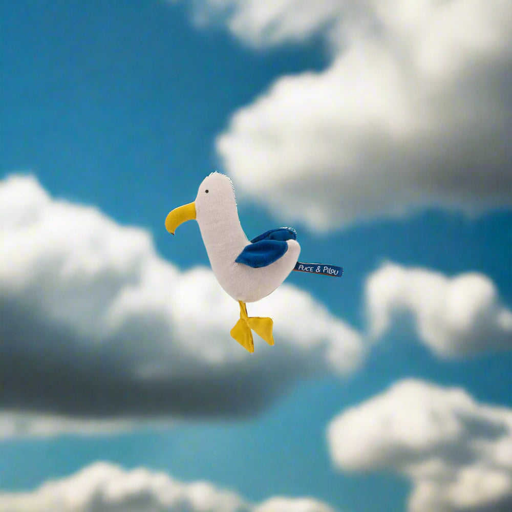 Plush toy rattle shaped like a seagull with white body, yellow beak and feet and blue wings