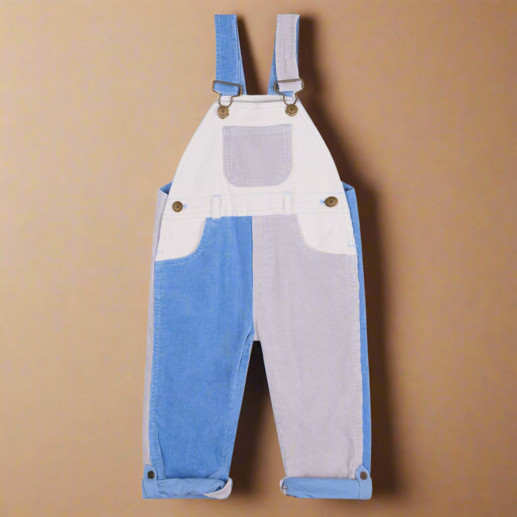 Patchwork corduroy dungarees in blocks of white, pale lilac and forget-me-not blue, with two side pockets and a central chest pocket with brass buttons
