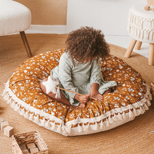 Child sitting on a round, patterned floor cushion in a cosy room