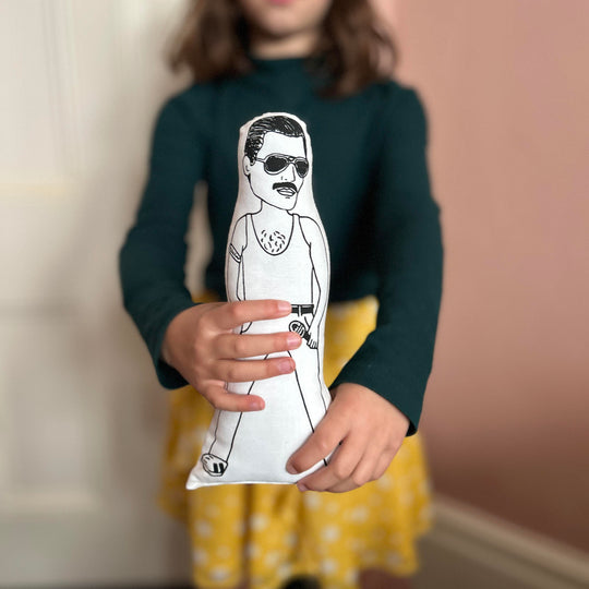 A child holding out a screen printed doll cushion of singer Freddie Mercury towards the camera