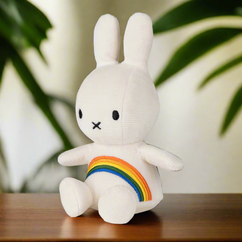 White plush toy toy rabbit with white corduroy fabric and an embroidered rainbow across the chest angled to the left