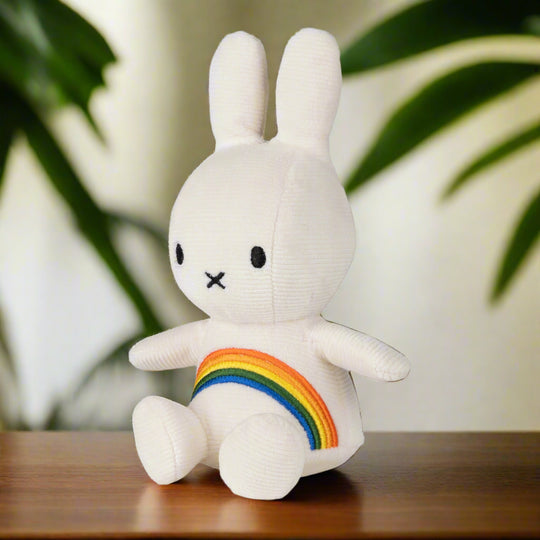 White plush toy toy rabbit with white corduroy fabric and an embroidered rainbow across the chest angled to the left