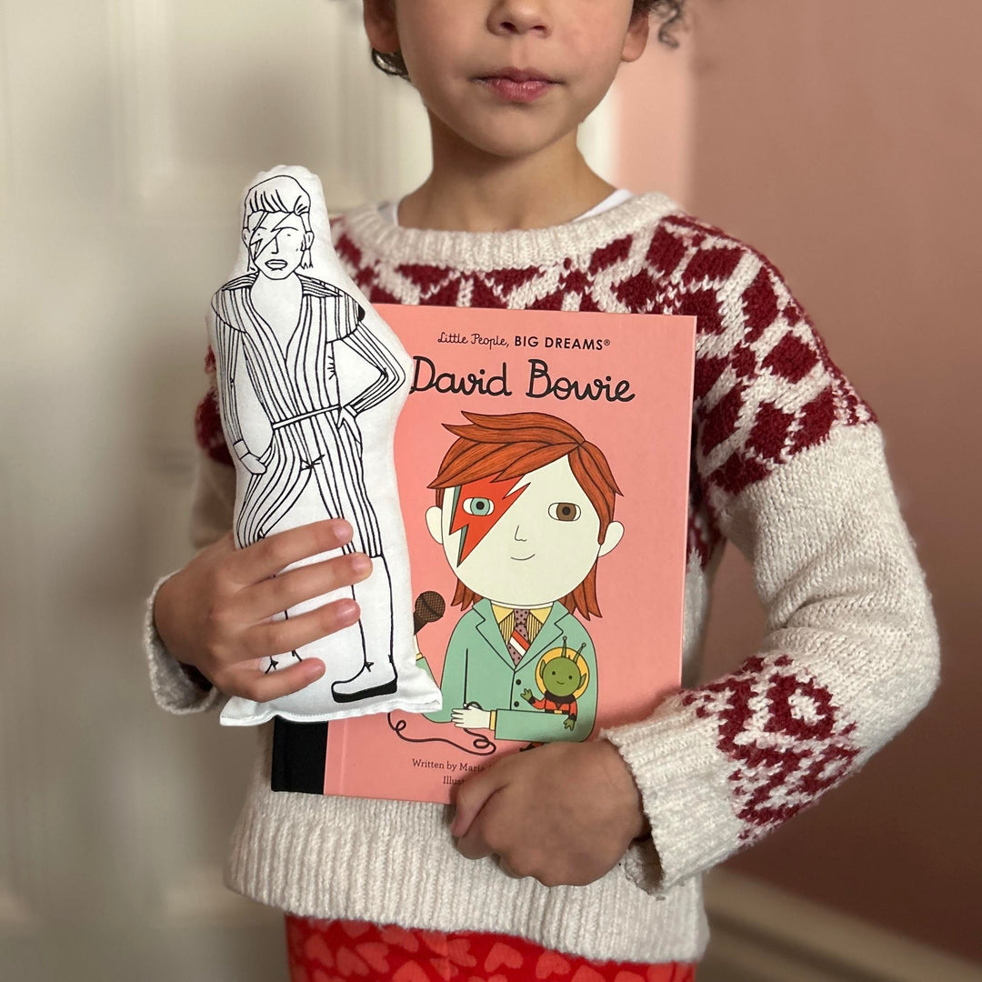 A child holding a screen printed doll cushion of David Bowie and alos a Little People Big Dreams book of David Bowie's life
