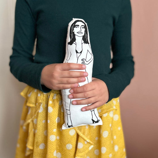 A child holding a screen printed fabric cushion doll with an illustration of PJ Harvey in her iconic cat suit.