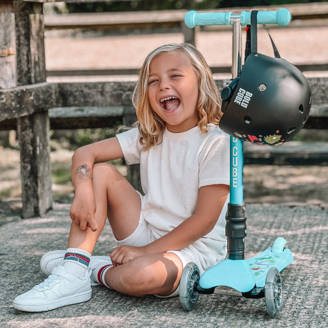 Child sitting on the ground with a light blue scooter and black helmet