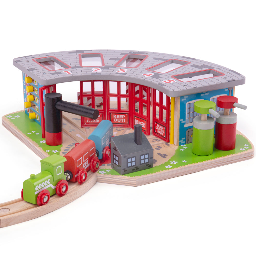 A colourful wooden toy train set featuring a five-way engine shed with train cars, a signal box, and other railway accessories.
