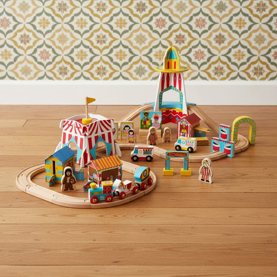 A colorful wooden train set depicting a fun fair theme, including a train engine and carriages, various fairground accessories, and wooden train tracks arranged in a looped circuit.