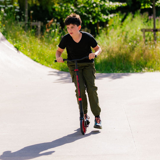 Child riding a scooter on a paved path with greenery in the background