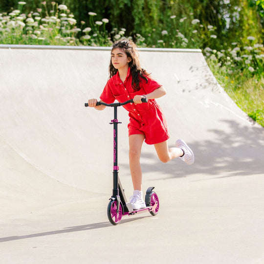 Girl in red outfit riding a scooter on a concrete surface with greenery in the background