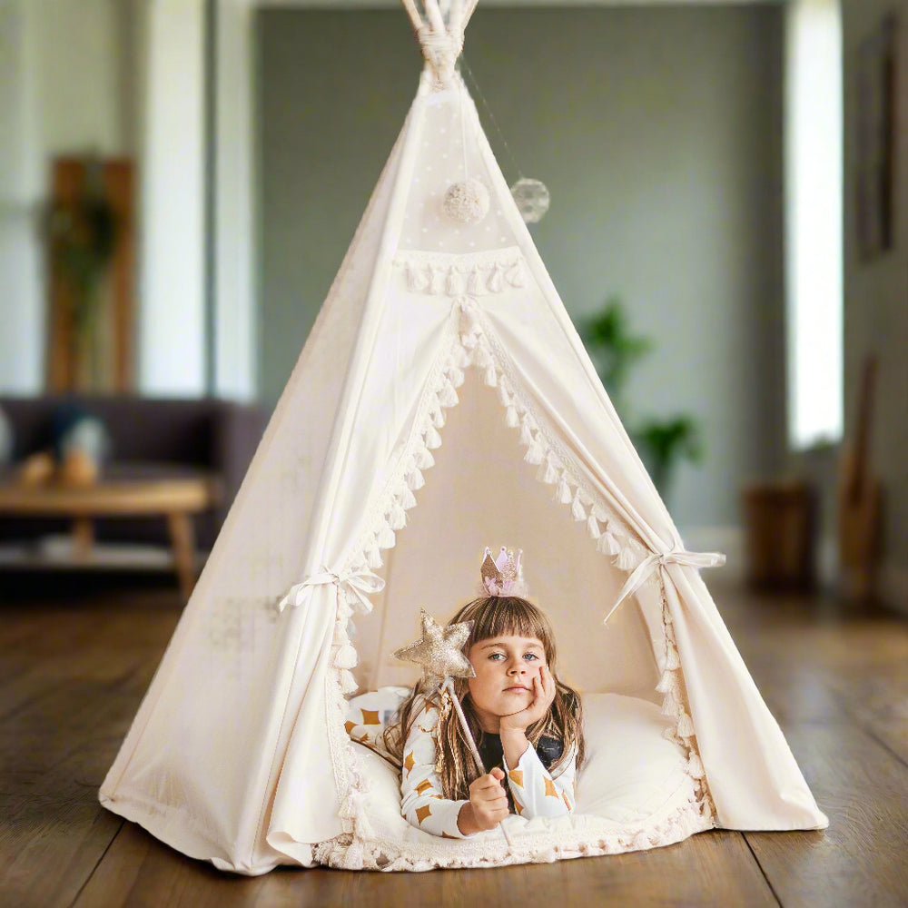 Child holding a star magic wand lying on a white round floor cushion with tassles inside a white teepee play tent