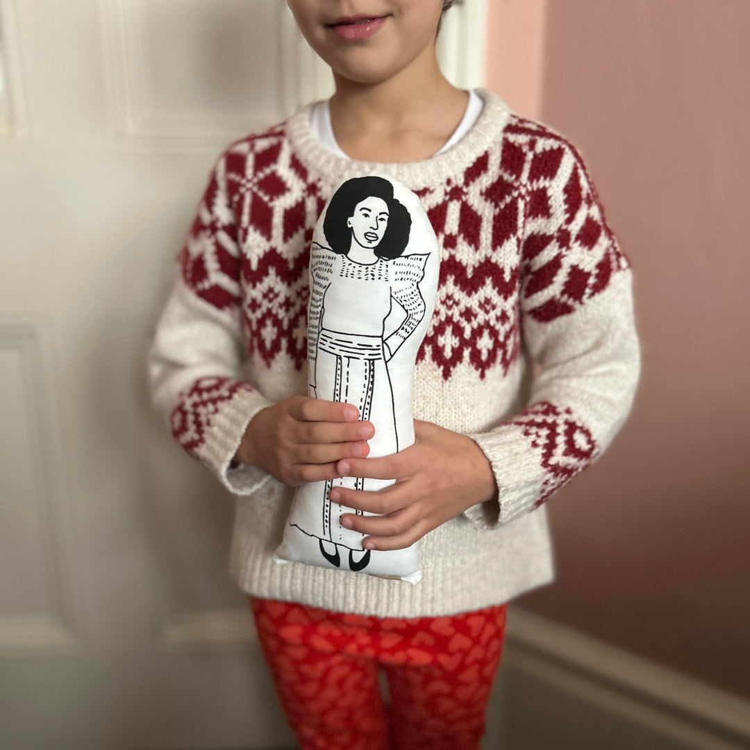 A chhild holding a screen printed doll cushion of Chimamanda Ngozi Adichie
