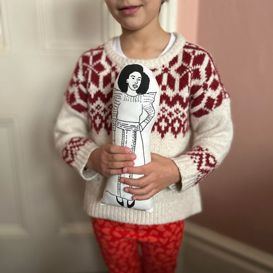 A chhild holding a screen printed doll cushion of Chimamanda Ngozi Adichie
