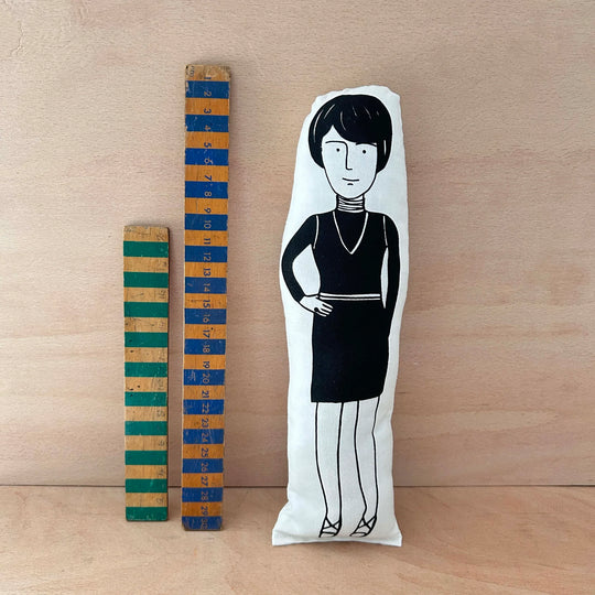 Screen printed doll cushion of Bridget Riley next to two wooden rulers on a wooden background