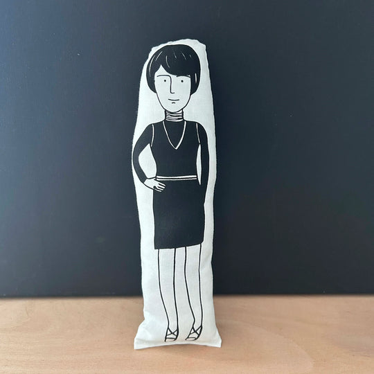 Screen printed doll cushion with white fabric and black illustration depicting artist Bridget Riley wearing a polo neck dress with one hand on hip