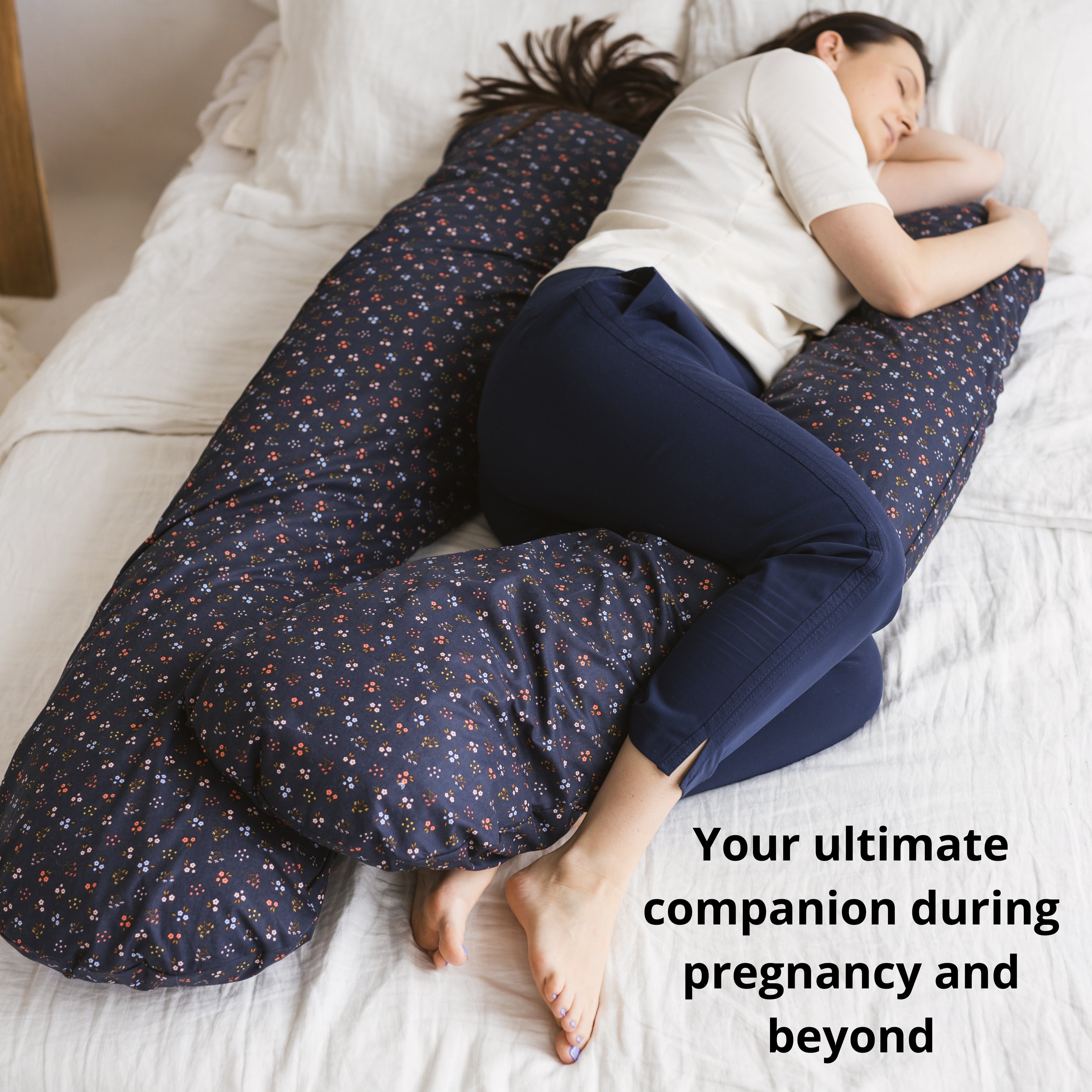 Woman lying on a bed with a U-shaped body pillow, surrounded by soft bedding.