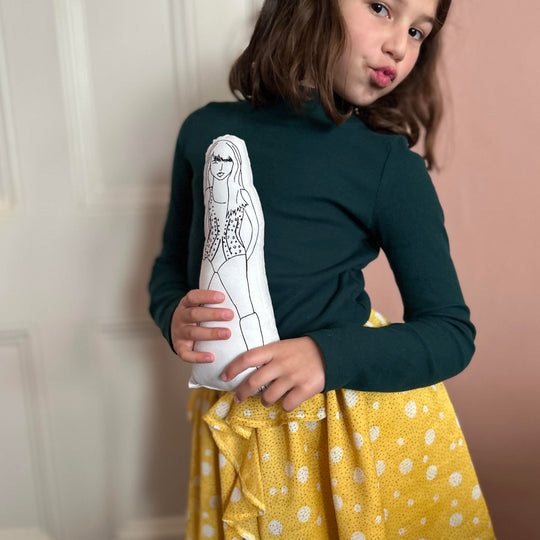 A child holding a screen printed doll of Taylor Swift while posing and pouting