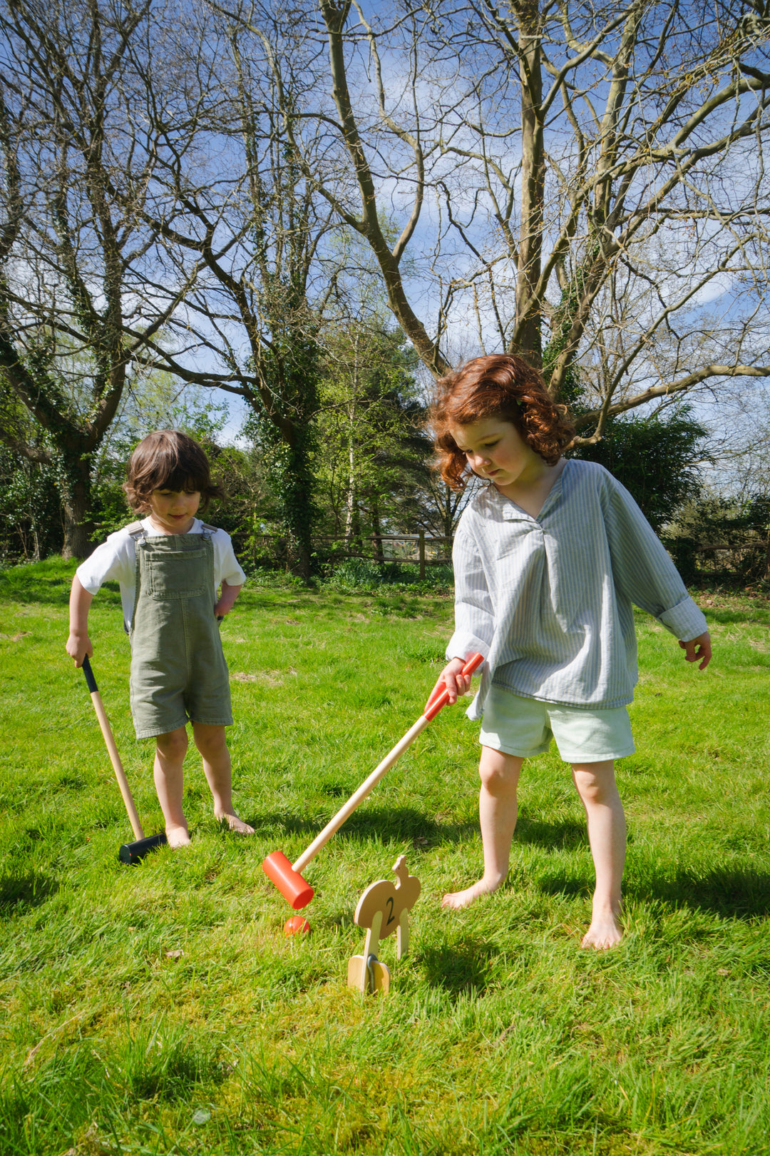 Two children playing with toys in a grassy field on a sunny day.