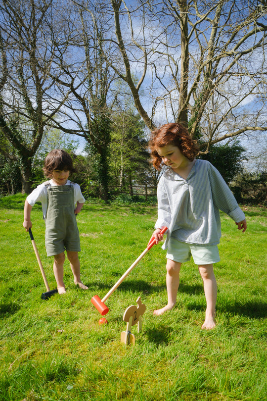 Two children playing with toys in a grassy field on a sunny day.