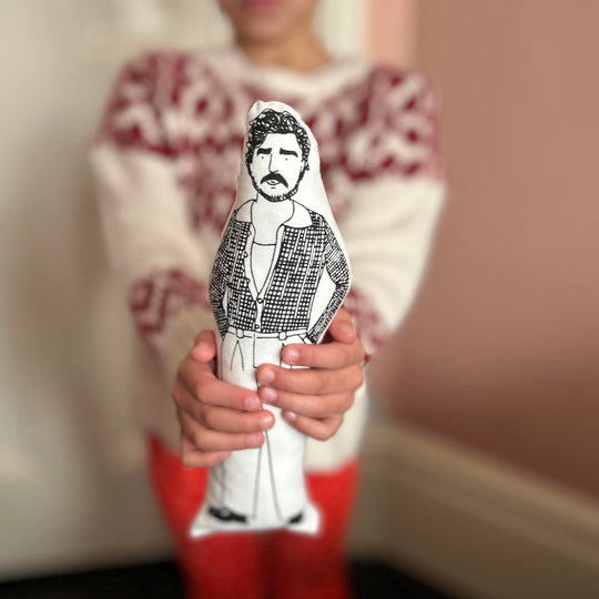 A child holding a black and white screen printed cushion doll depicting an illustration of Pedro Pascal.