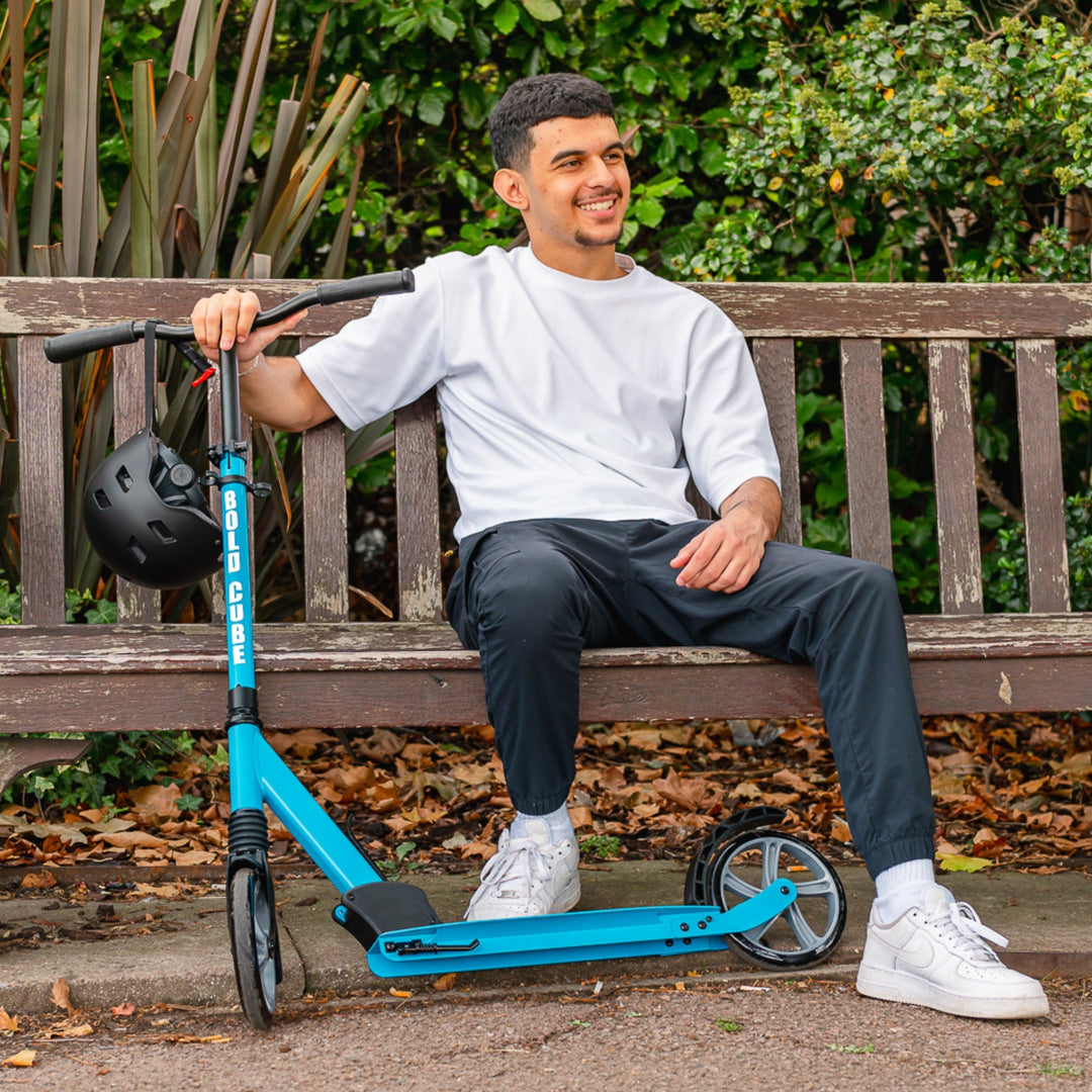 Man sitting on a bench with a blue scooter, with a black helmet hanging off the handlebar