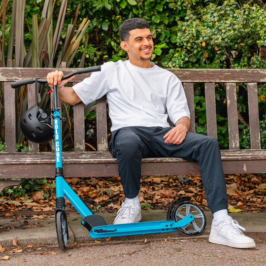Man sitting on a bench with a blue scooter, with a black helmet hanging off the handlebar