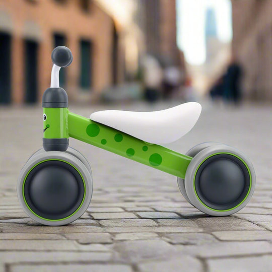 Green and grey balance bike with a white seat on a cobbled pavement background
